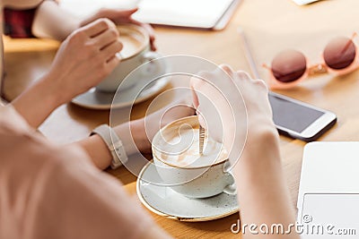 Close-up partial view of young women sitting at table and drinking coffee Stock Photo