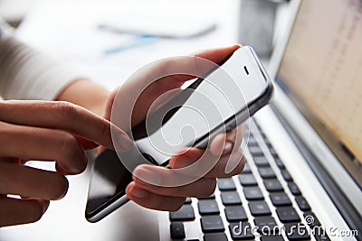 Close Up Of Person At Laptop Using Mobile Phone Stock Photo