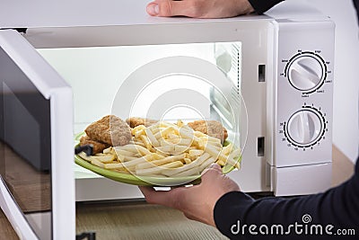 Person Putting Fried Food Inside Microwave Oven Stock Photo