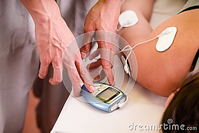 Close-up of a personal trainer touching with one hand the electric machine with the electrostimulator electrodes in the Stock Photo