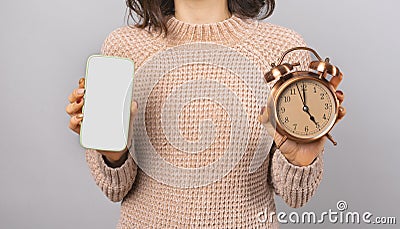 Close up phot of woman showing blank screen on smartphone and alarm clock over grey background Stock Photo