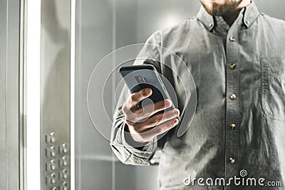 Close up photo of a busy man using smartphone in the elevator. Ambitious office worker texting by her phone in the lift. Focus on Stock Photo