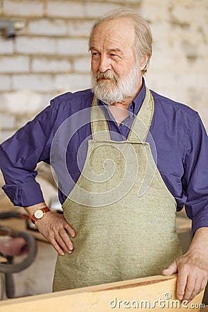 Close up photo of cheerful old joiner holding woodenplank workstation Stock Photo