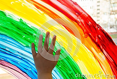 Close-up photo of child`s hand touch painting rainbow on window. Family life background. Image of kids leisure at home Stock Photo