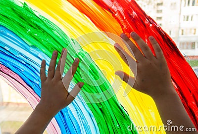 Close-up photo of child`s hands touch painting rainbow on window. Family life background. Image of kids leisure at home Stock Photo