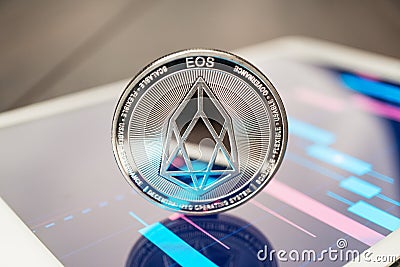 Close-up photo of eos cryptocurrency physical coin on the tablet computer showing stock market charts. trading eos cryptocoin Editorial Stock Photo