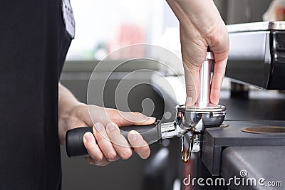 close-up photo of female hands holding a metal tamper and a portafilter with coffee in a coffee shop. Stock Photo