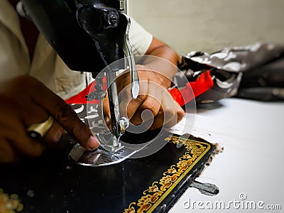 Close up photo of manual sewing machine with tailor hands stitching red cloth with selective focus Stock Photo