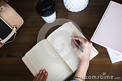 Close-up photo of scheduler notebook on a wooden table. Female hand writes on paper. Stock Photo