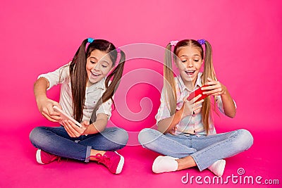 Close up photo two people little age she her girls hold hands arms telephones sit floor involved video games wear casual Stock Photo