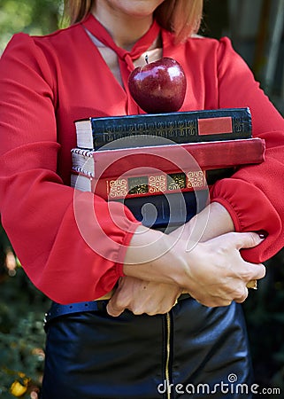 Close-up picture of hands, holding a bunch of books and red apple. Female student, wearing red shirt and black skirt, with many Stock Photo