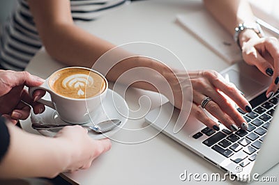 Close up picture of hands of a waiter giving a cup of cuppuccino to a woman typing with a keyboard. Stock Photo