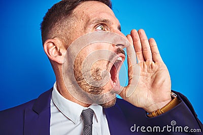 Close up picture of young handsome business man over blue isolated background shouting and screaming loud to side with hand on Stock Photo