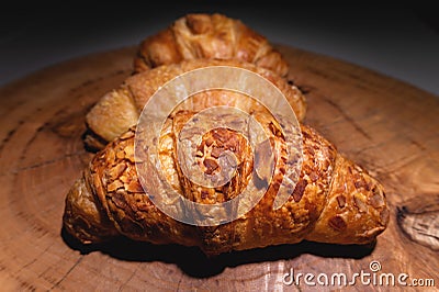 Close-up of a pile of three croissants on a wooden board against a dark background. Delicious and healthy breakfast Stock Photo