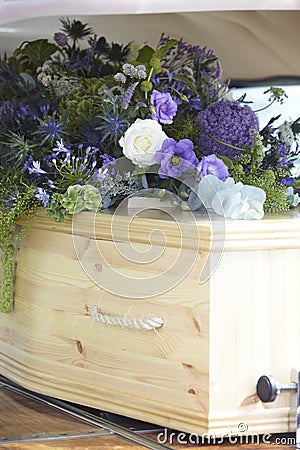 Close Up Of Plain Wooden Coffin With Floral Tributes In Back Of Hearse At Funeral Stock Photo