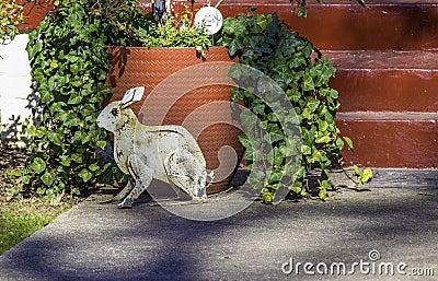 Red painted steps, a big red pot spilling over with ivy, and a metal rabbit sculpture make a playful garden scene Stock Photo