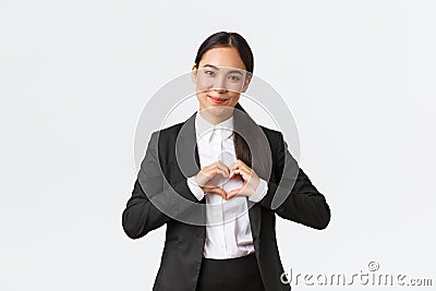 Close-up of pleasant asian businesswoman, saleswoman in black suit care for her clients, showing heart sign and smiling Stock Photo