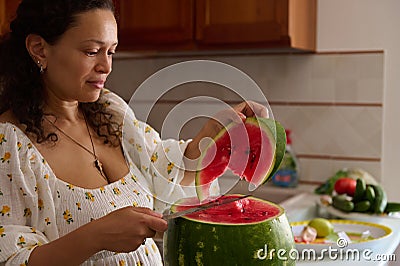 Close-up of a pleasant housewife cutting ripe organic juicy watermelon in the rustic home kitchen interior Stock Photo