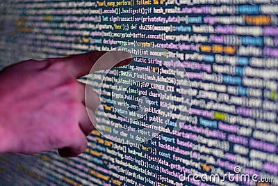 Close-up of a pointing hand over a large, glowing display screen filled with colorful code, possibly representing Stock Photo