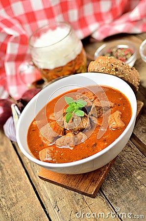 Close-up of pork goulash with pieces of meat in a bowl, garlic, pepper, onion, glass with cold beer and red checkered Stock Photo