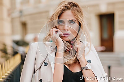 Close-up portrait of adorable blonde girl with pink lipstick playfully posing on blur street background. Blue-eyed Stock Photo
