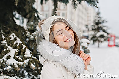Close up portrait of amazing joyful girl in white warm warm clothes enjoying winter time in city. Young pretty woman in Stock Photo