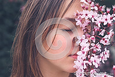 Close up portrait of attractive romantic teenage girl smelling aroma of blooming spring pink plum tree flowers with closed eyes. Stock Photo