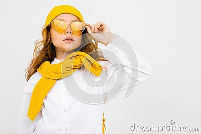 Close-up portrait of an attractive smiling girl in a yellow hat and sunglasses, in a white shirt with a tied sweater on Stock Photo