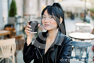 Close-up portrait of attractive stylish smiling Asian girl with brunette ponytail hair, wearing casual black leather Stock Photo