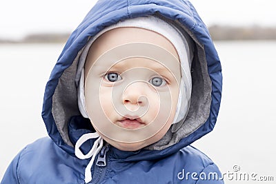 Close-up portrait of baby boy looking at camera. Cute infant boy in a hat and a hood. Outdoor shot Stock Photo