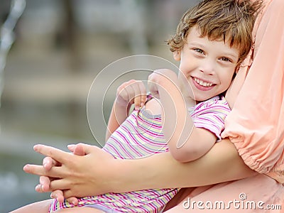 Close-up portrait of beautiful disabled girl in the arms of his mother having fun in fountain of public park at sunny summer day. Stock Photo