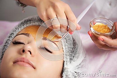 Close-up of portrait of beautiful girl applying gold facial mask Stock Photo