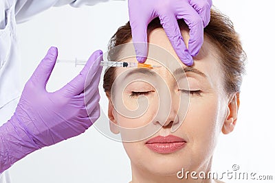 Close-up portrait of a beautiful middle age woman and doctor hands making botox injection isolated on white background. Collagen. Stock Photo