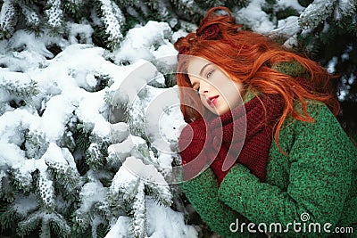 Close up portrait of a beautiful red-haired girl leaning on snowy fir tree bough with dreaming look. Stock Photo