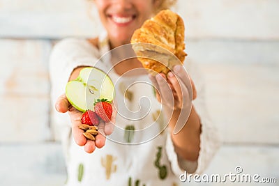 Close up and portrait of beautiful woman showing at the camera healthy food like fruit and in the other hand bad alimentation like Stock Photo