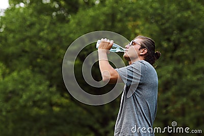 Handsome young sportsman drinking water out of bottle after running workout at public park. Taking break after hard workout Stock Photo