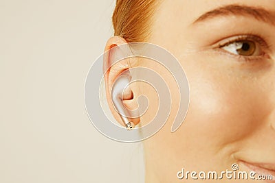 Close-up portrait of charming redhead caucasian woman with happy smile listening music with wireless earphone in ear. Stock Photo
