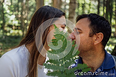 A close-up portrait of a charming woman and a man with a fern in the forest. A couple in love hide their faces under a green leaf Stock Photo