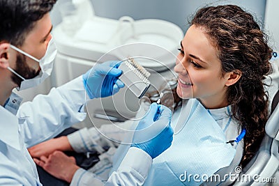 Close up portrait of charming young woman sitting in dental chair while stomatologist selecting color tone of her teeth Stock Photo