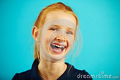 Close-up portrait of cheerful laughing girl with red hair and freckles on blue isolated background. Happy child Stock Photo