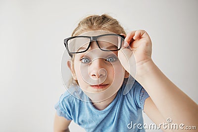 Close up portrait of cheerful small girl with blonde hair and blue eyes funny imitates adult person with glasses with Stock Photo