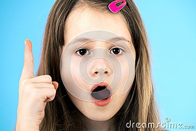 Close up portrait of a child school girl holding up point finger in I have an idea gesture isolated on blue background Stock Photo