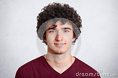 Close up portrait of curly handsome European male, wearing casual maroon shirt, isolated over white background, looking directly Stock Photo