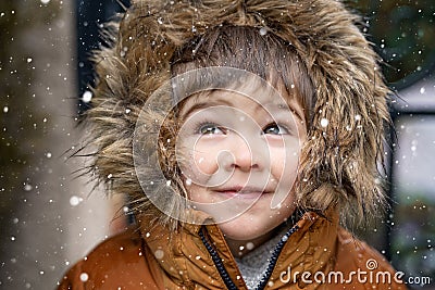 Close up portrait of cute little toddler boy in furry hood looking at snowfall Stock Photo