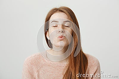 Close-up portrait of cute and tender redhead woman standing with closed eyes and pleased expression, folding lips and Stock Photo