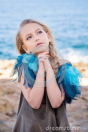 Close-up portrait of a cute young blond girl making a wish with hands clasped in fists in a dreamy pose on the sea Stock Photo