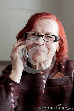 Close-up portrait of elderly woman with red hair, wearing eyeglasses. grandmother calls on phone, waits for an answer, listens, Stock Photo