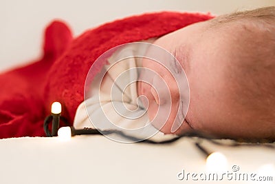 Close Up Portrait First Days Of Life Newborn Cute Funny Sleeping Baby In Santa Hat Wrapped In Red Diaper At White Stock Photo