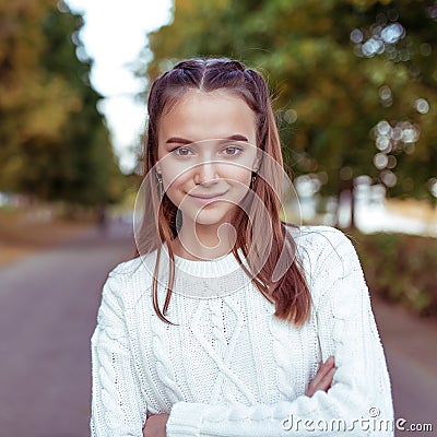 Close-up portrait of girl, teenager schoolgirl, in white knitted sweater, in summer in park. Happy smiles, emotions of Stock Photo
