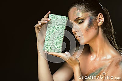 Close up portrait of gorgeous woman with closed eyes and artistic snakeskin make up holding green leather purse at her face Stock Photo